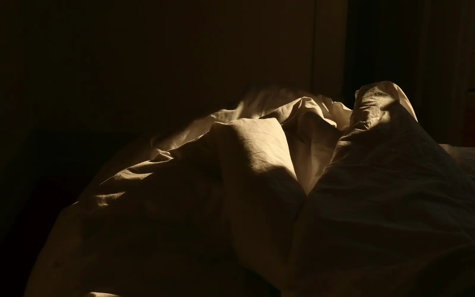 Cama desfeita atravessada por uma faixa de luz da manhã