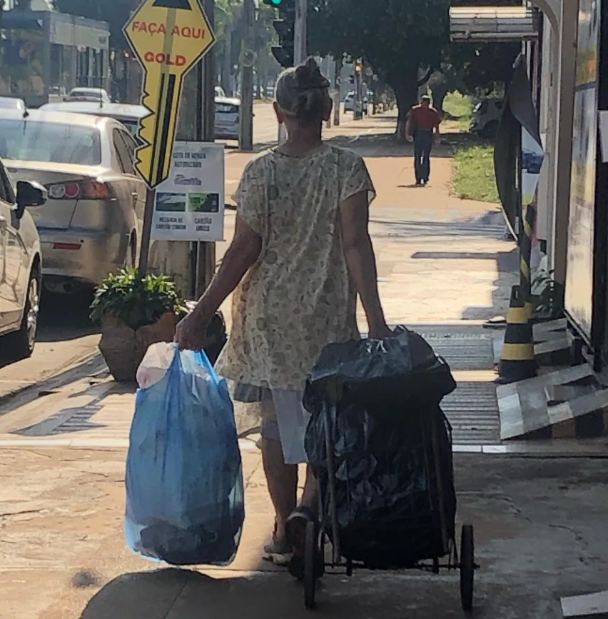 Mulher caminhando pela calçada com sacolas e um carrinho